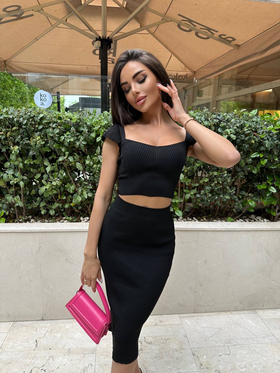Woman in a black outfit holding a pink clutch outdoors