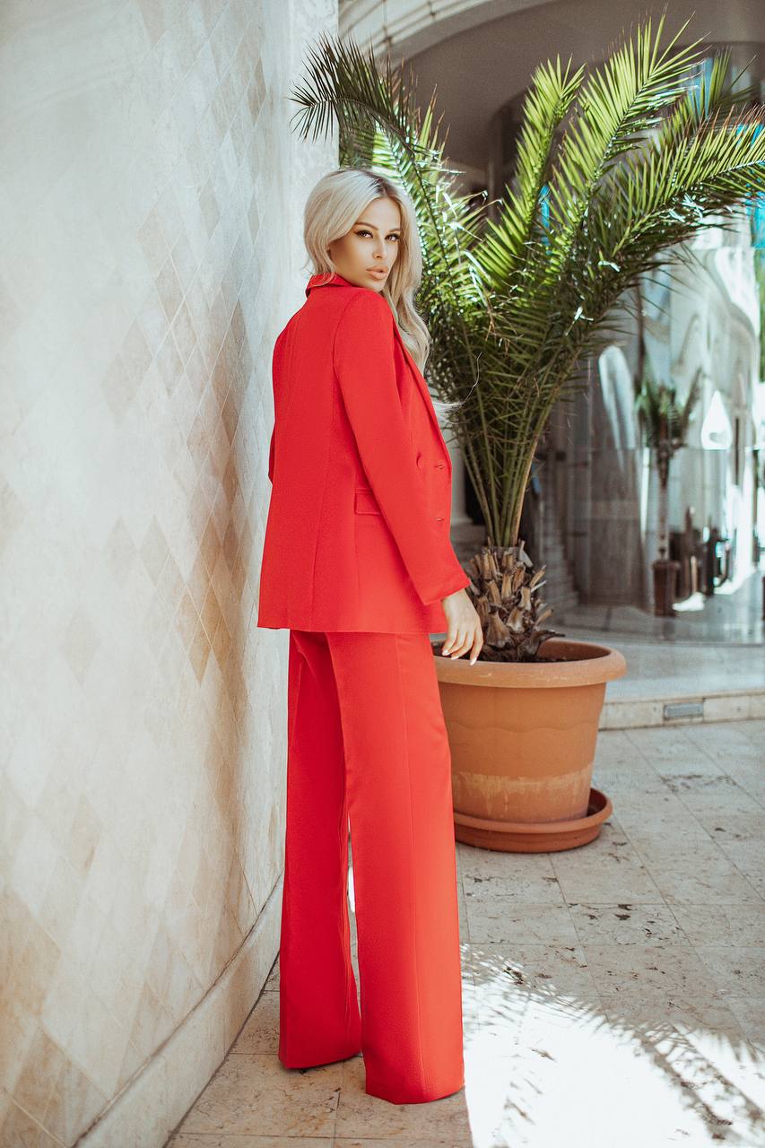 Woman in a red suit standing next to a potted plant in an outdoor setting