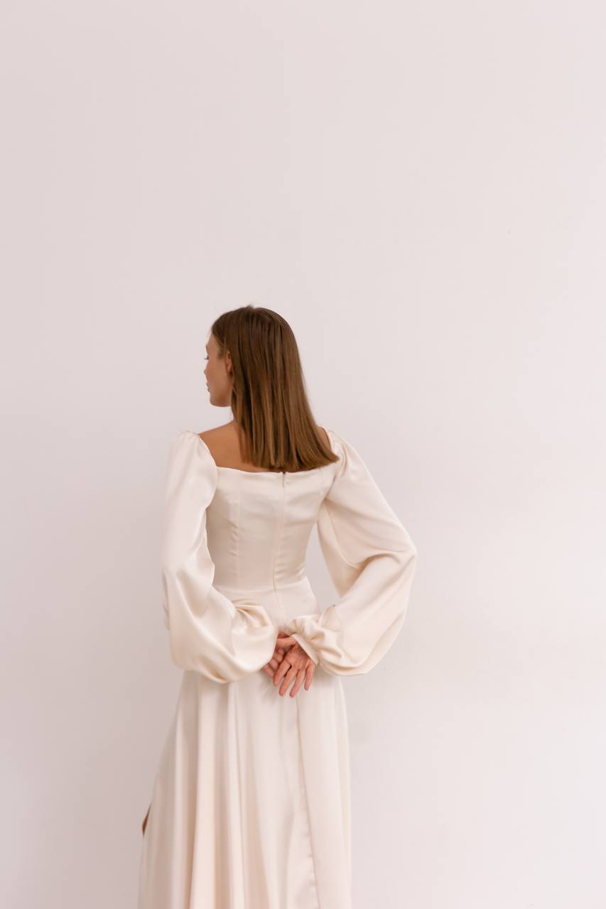 Woman wearing a white dress with long sleeves against a plain background