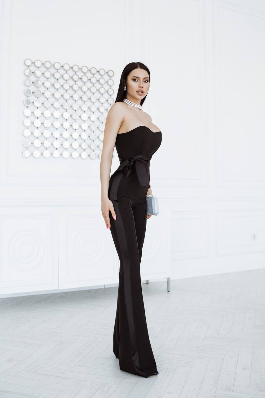 Woman in a black strapless gown standing against a white wall.