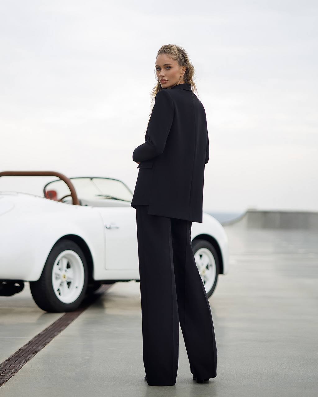 Person wearing a black outfit standing in front of a white vintage car.
