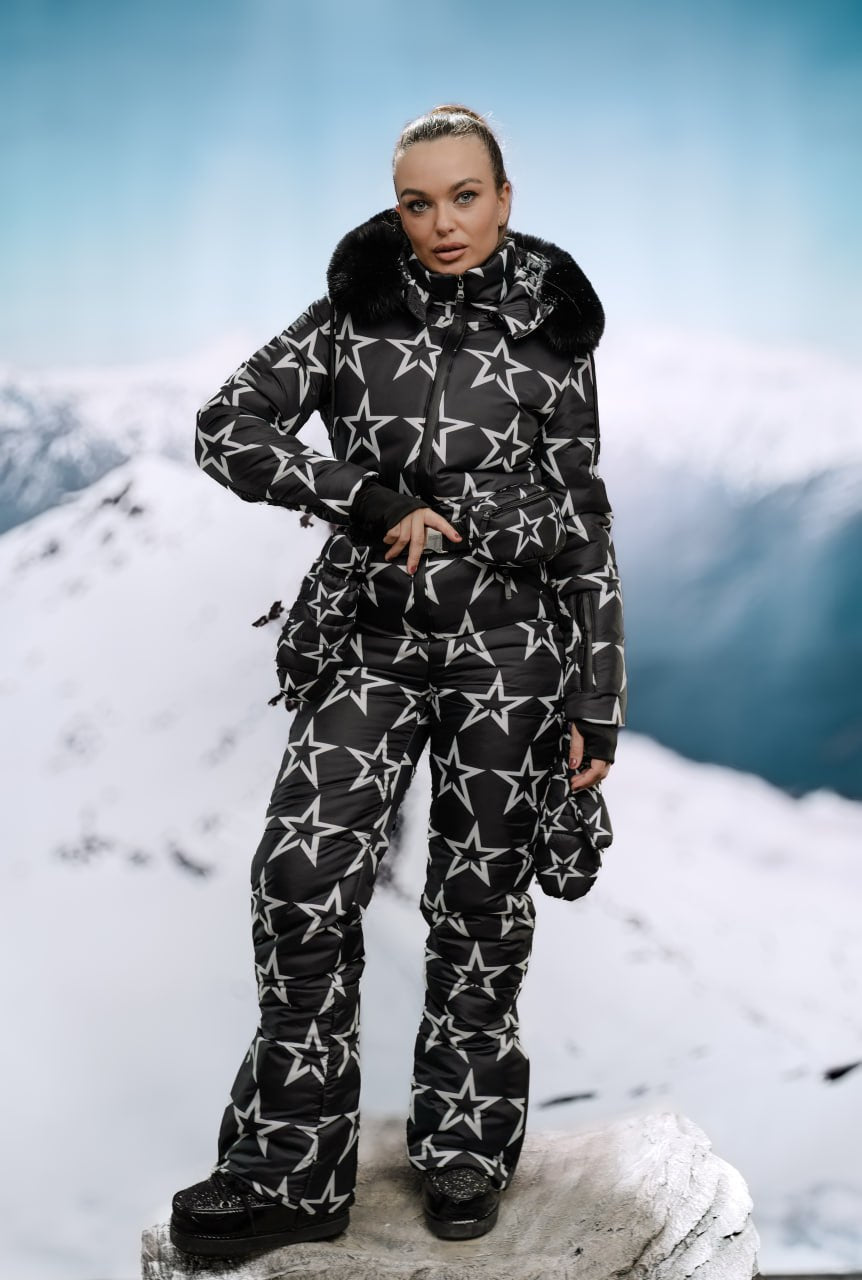 Person wearing a black and white star-patterned snowsuit on a snowy mountain background