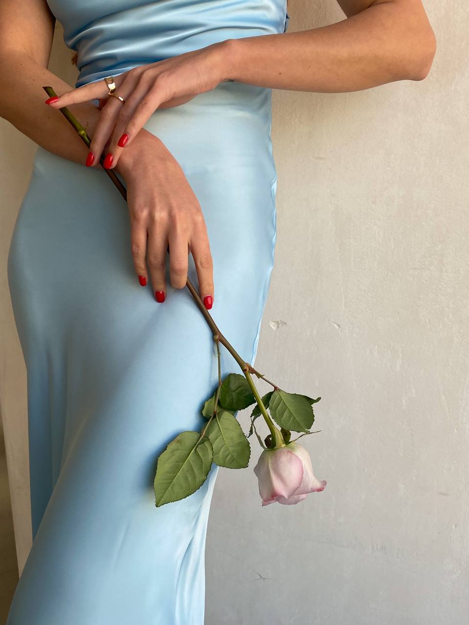 Person wearing a light blue dress holding a pink rose against a plain background