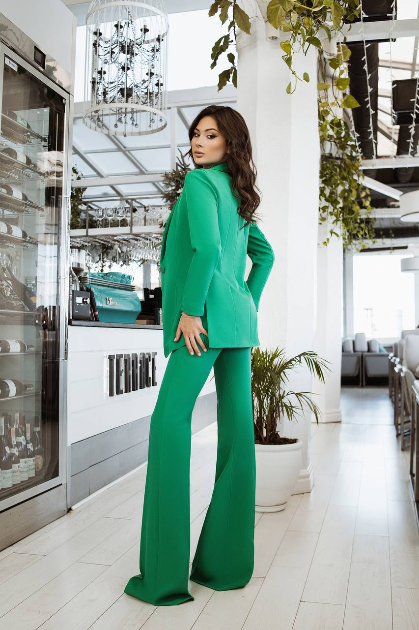 Woman in a green suit standing in a modern indoor setting with plants and decor.