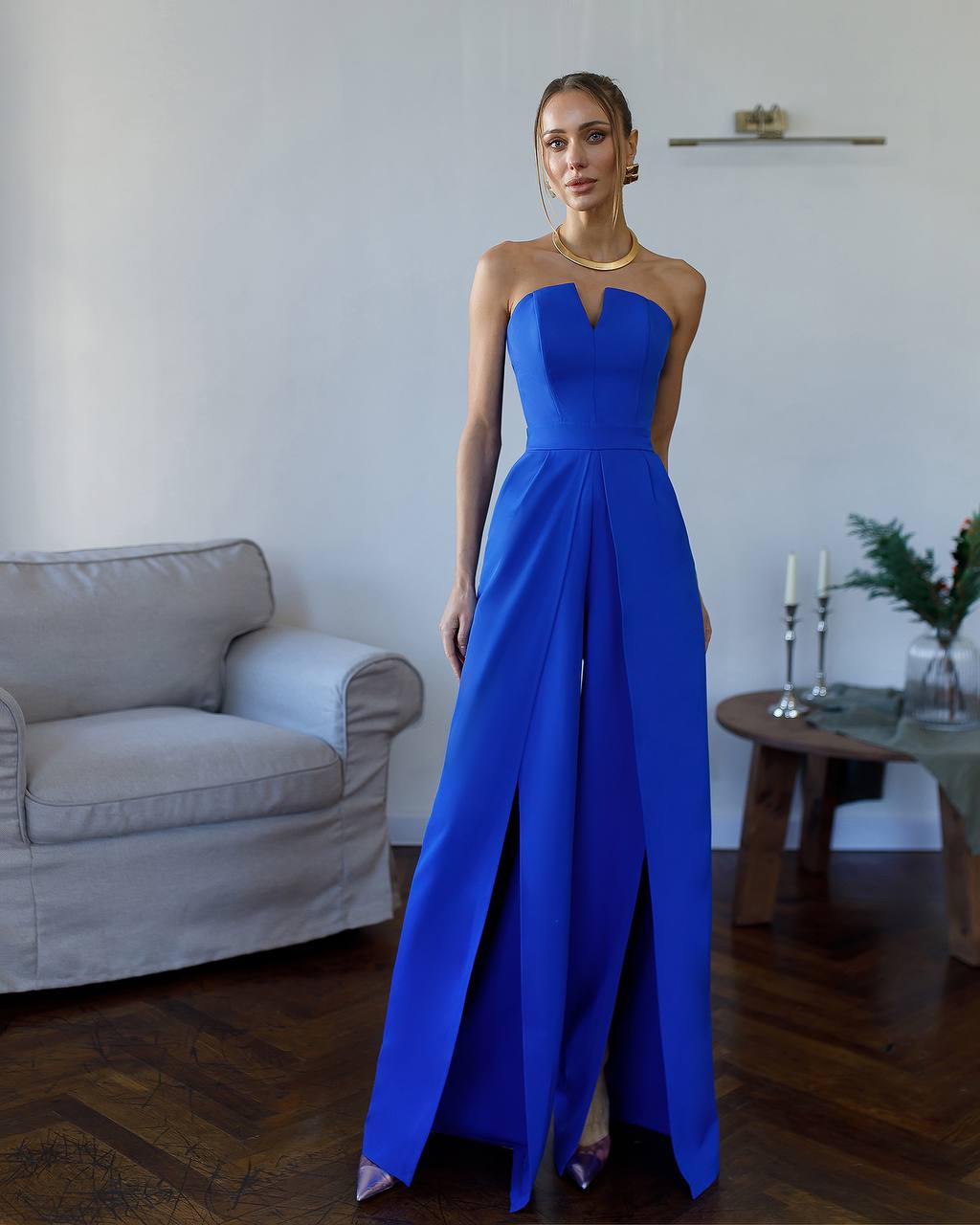 Woman in a blue strapless gown standing in a room with a couch and table.