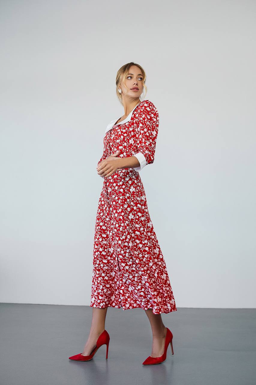Woman wearing a red floral dress with red high heels on a plain background