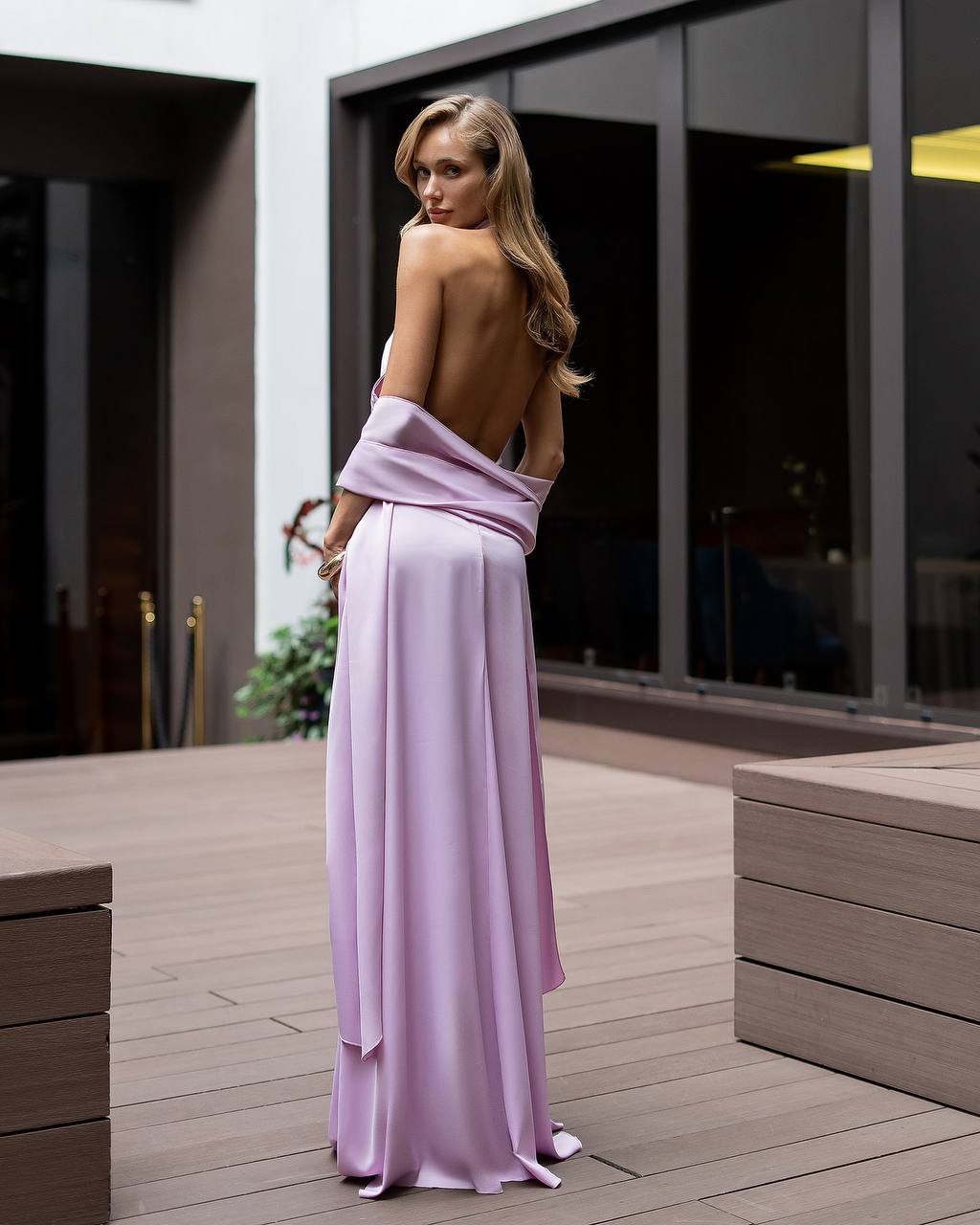 Woman in a long, light purple dress standing on a wooden deck.