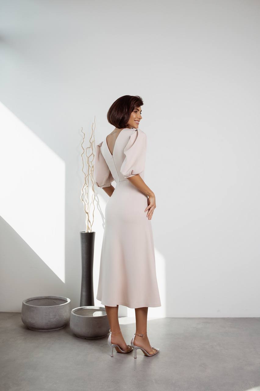 Woman in a white dress standing in a minimalistic room with a vase and plant.