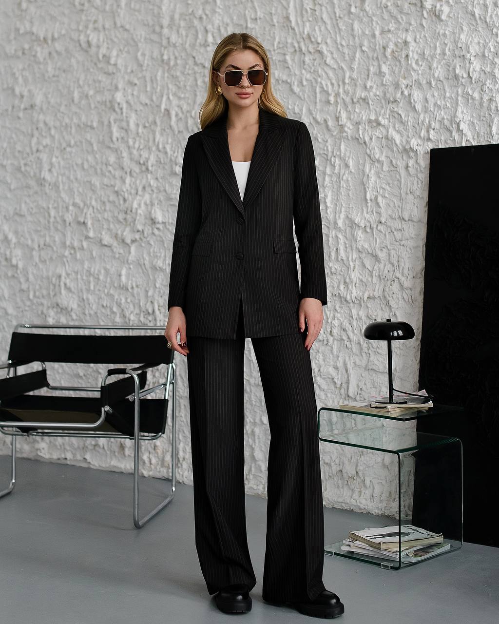Woman in a black pinstripe suit standing in a modern interior setting.
