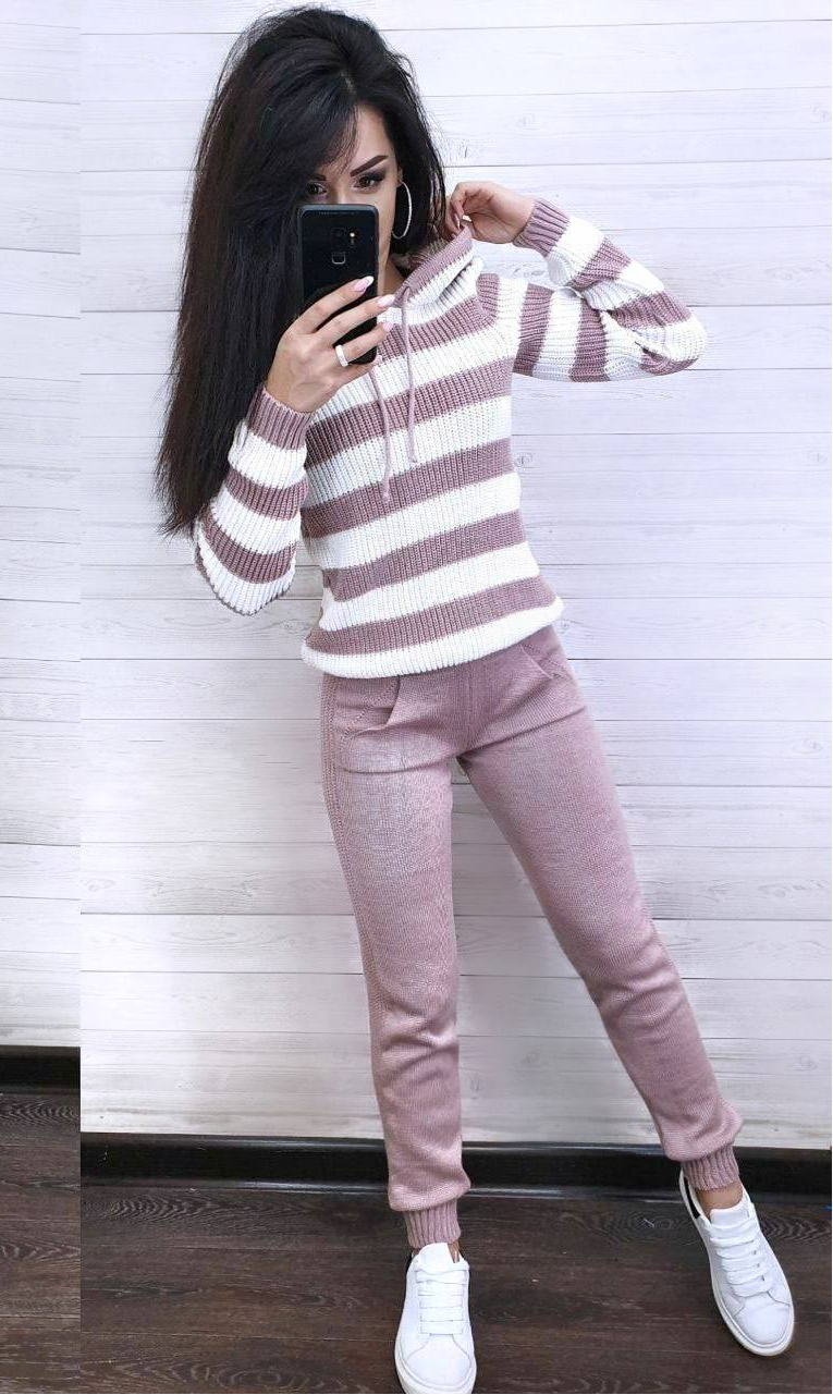 Person wearing a striped sweater and pink pants against a white wall.