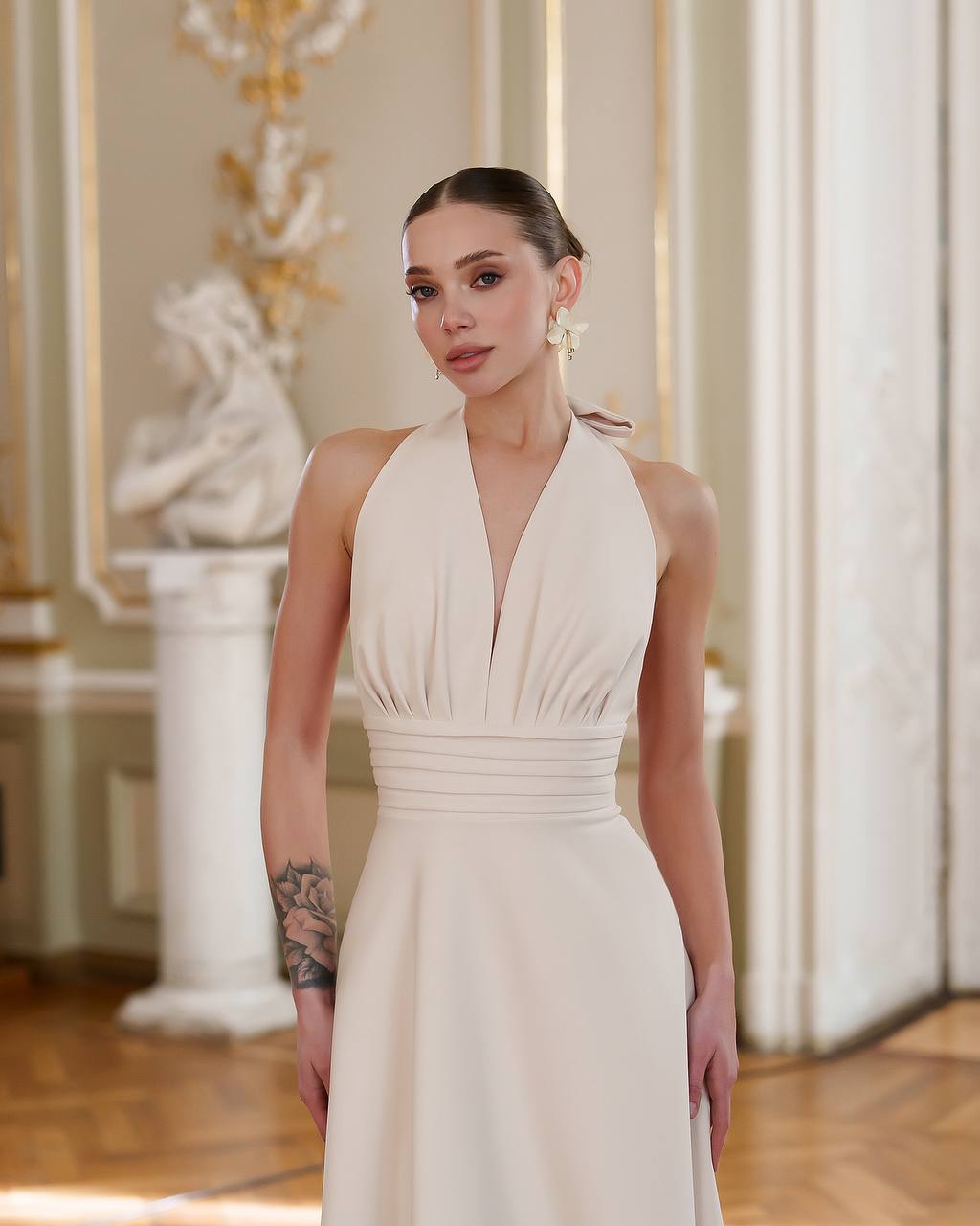 Woman in a white halter-neck dress standing in an elegant interior setting.
