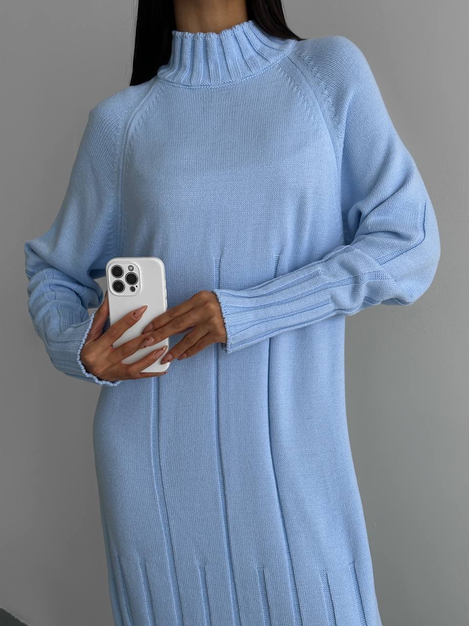 Person wearing a long light blue sweater holding a phone on a gray background