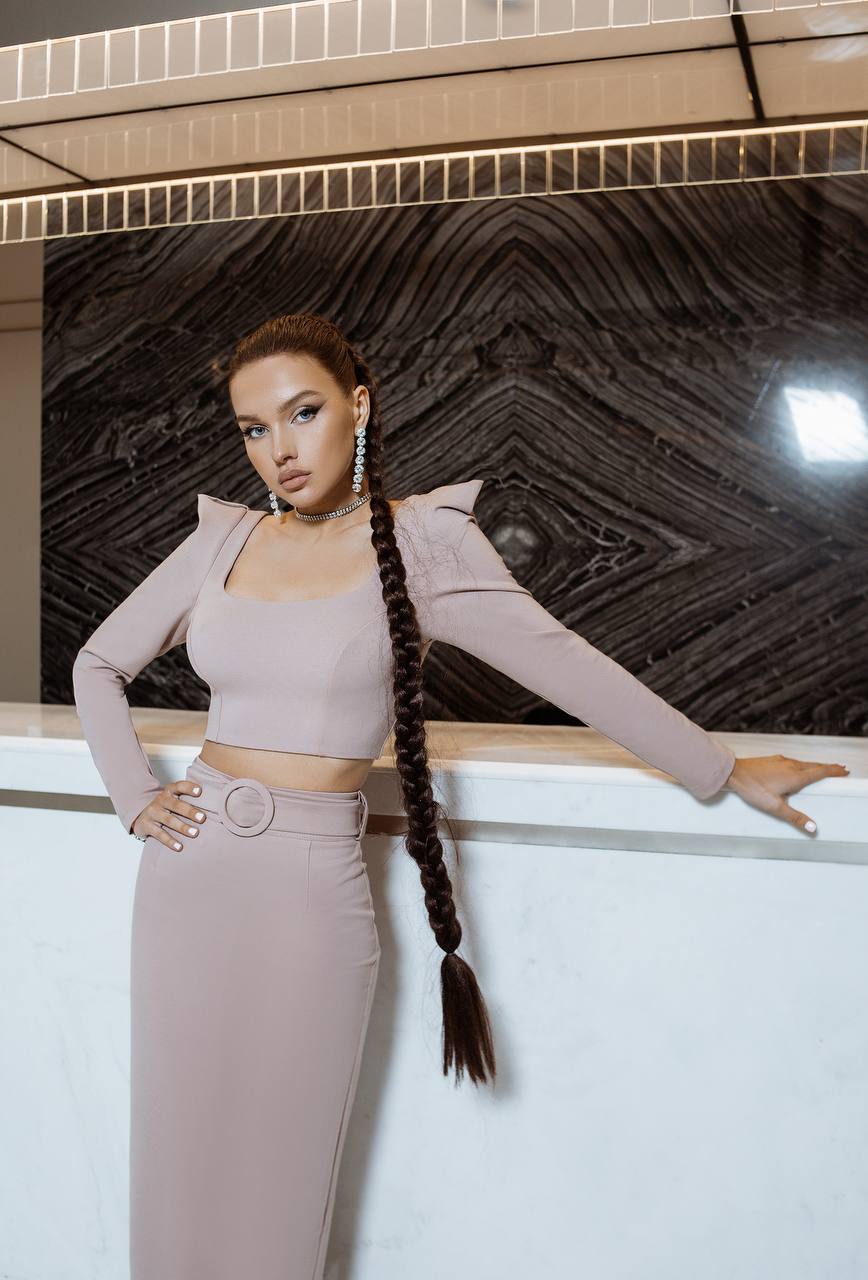 Woman in a stylish outfit with a long braid standing against a decorative wall.