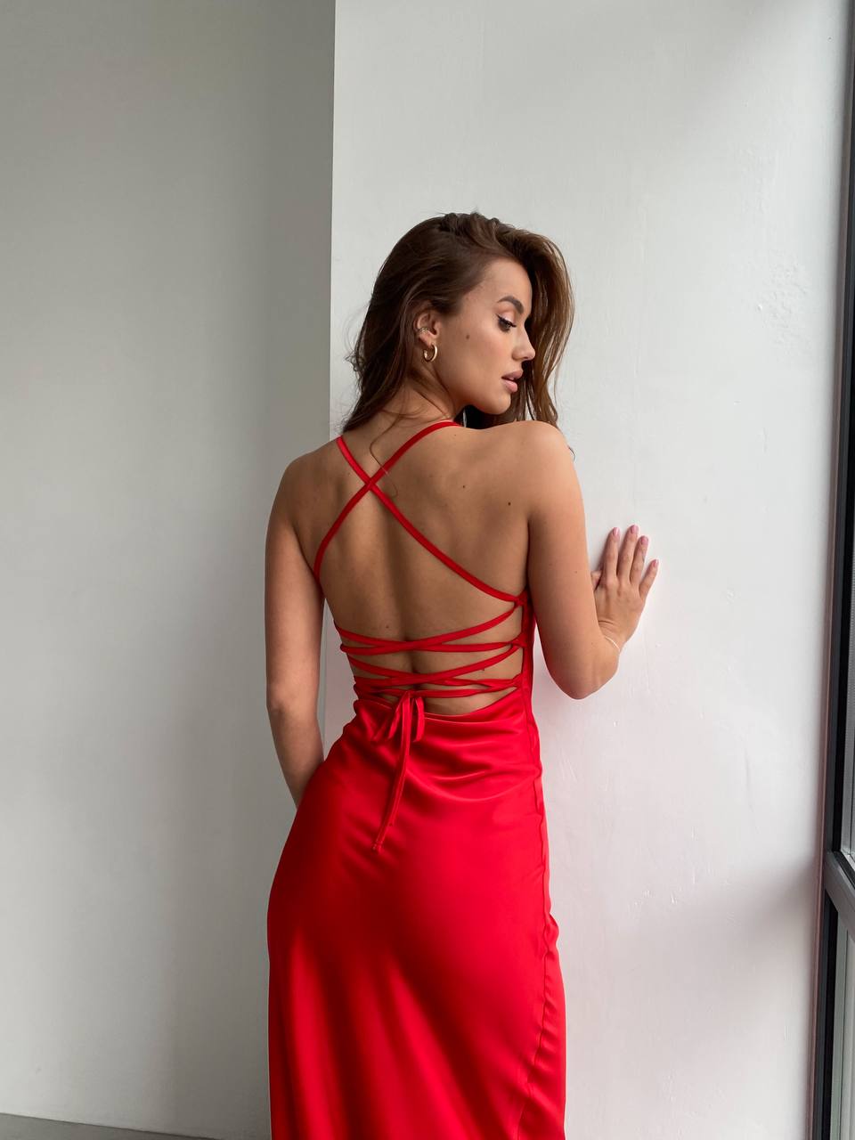 Woman wearing a red dress with thin straps against a white wall