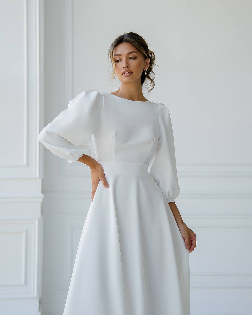 Woman wearing a white dress with long sleeves against a white wall