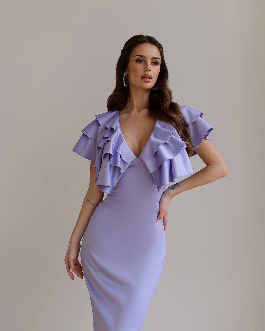 Woman wearing a lavender dress with ruffled shoulders against a plain background
