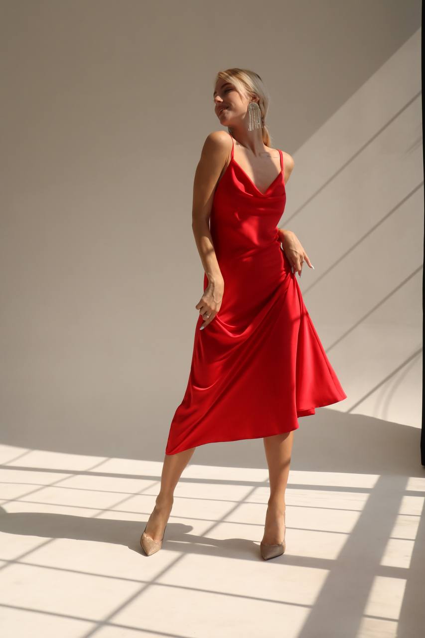 Woman wearing a red dress standing in a well-lit room with sunlight casting shadows on the floor.