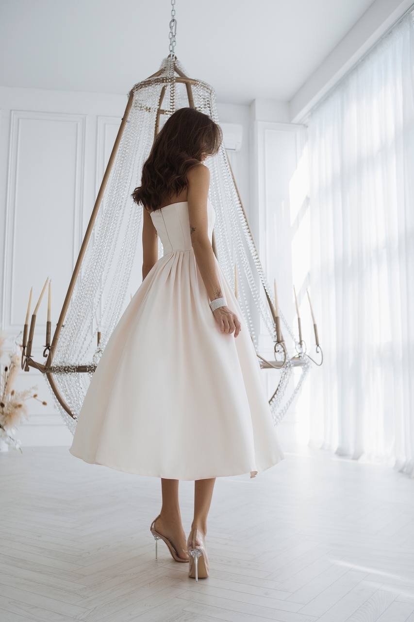 Woman in a white dress standing in a bright room with a large window and decorative elements.