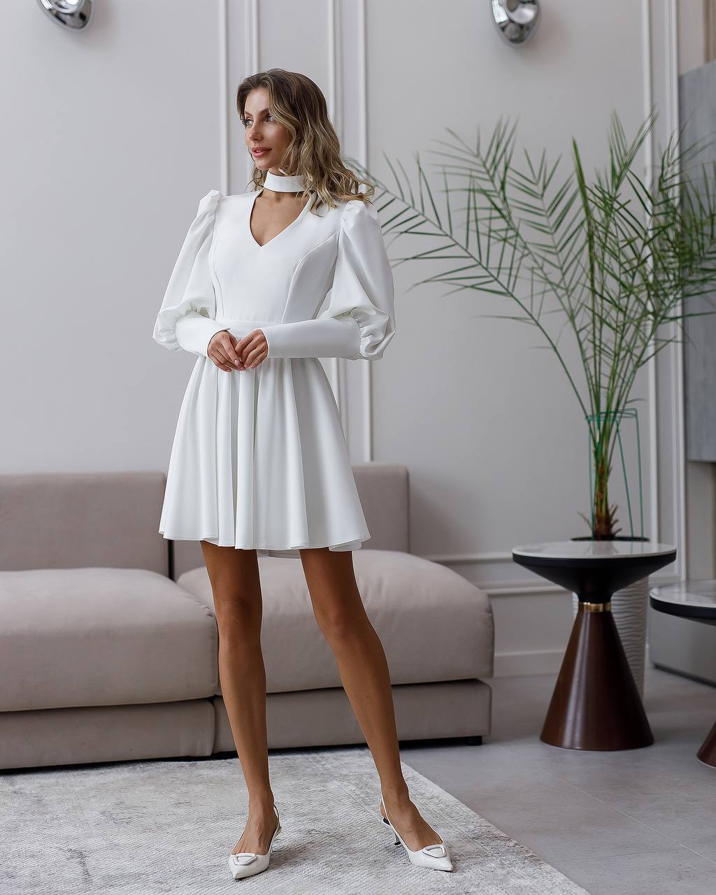 Woman in a white dress standing in a modern living room.