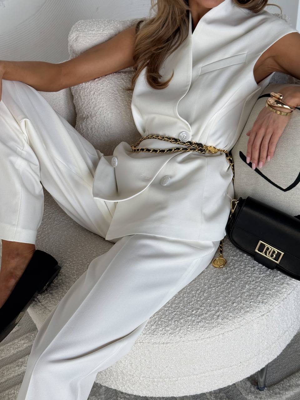 Person wearing a white outfit with a gold chain, sitting on a textured surface.