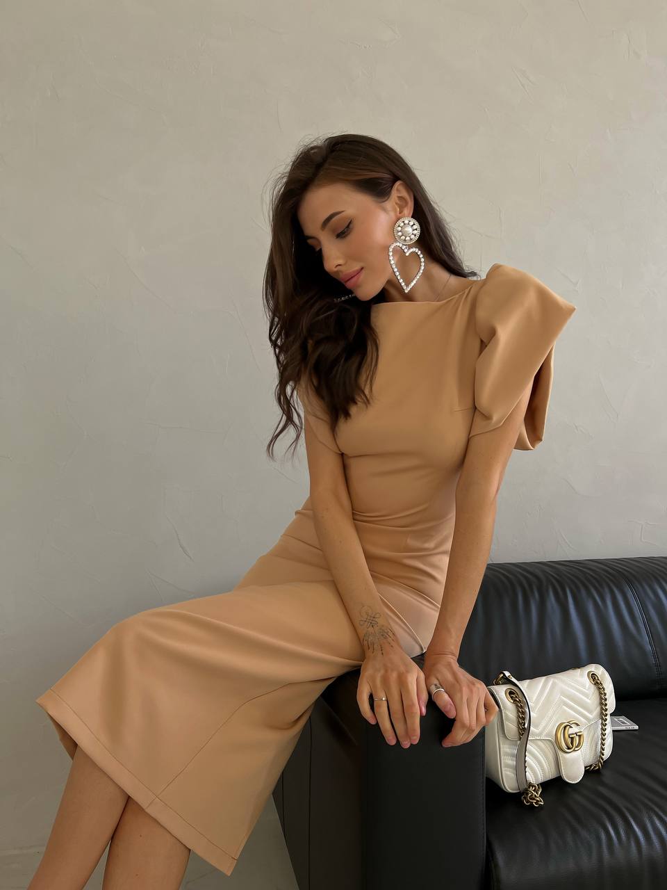Woman in a beige dress sitting on a black couch with a white handbag.