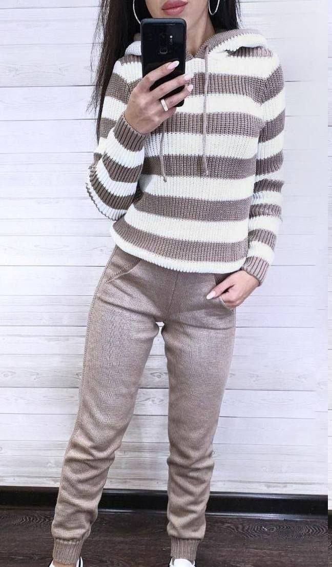 Person wearing a striped sweater and beige pants against a white wall.