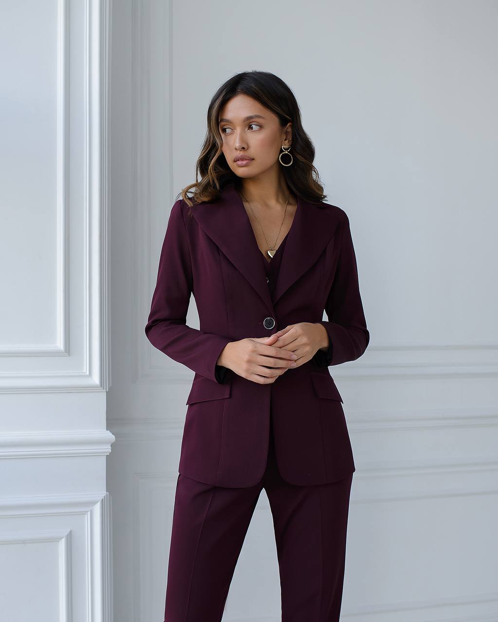 Woman wearing a burgundy suit standing against a light gray wall.