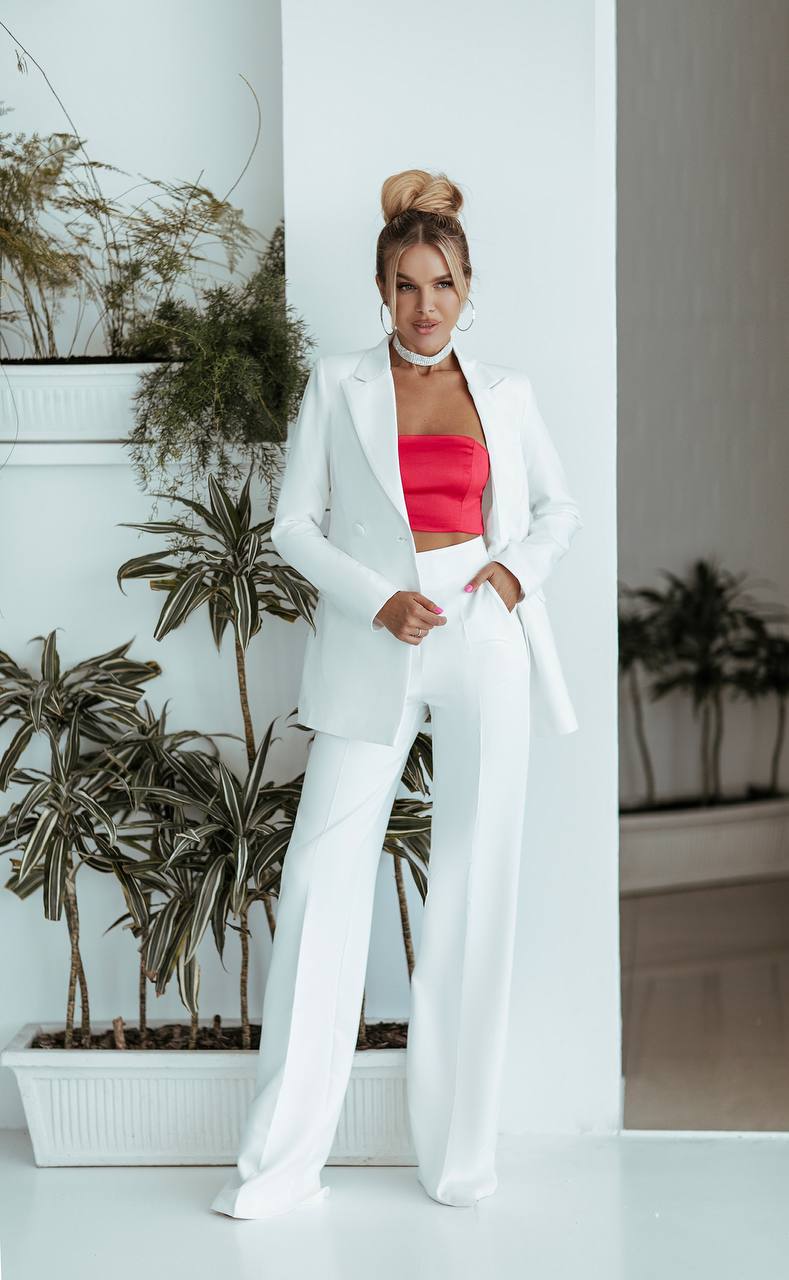 Woman in a white outfit with a red top standing in a room with plants.