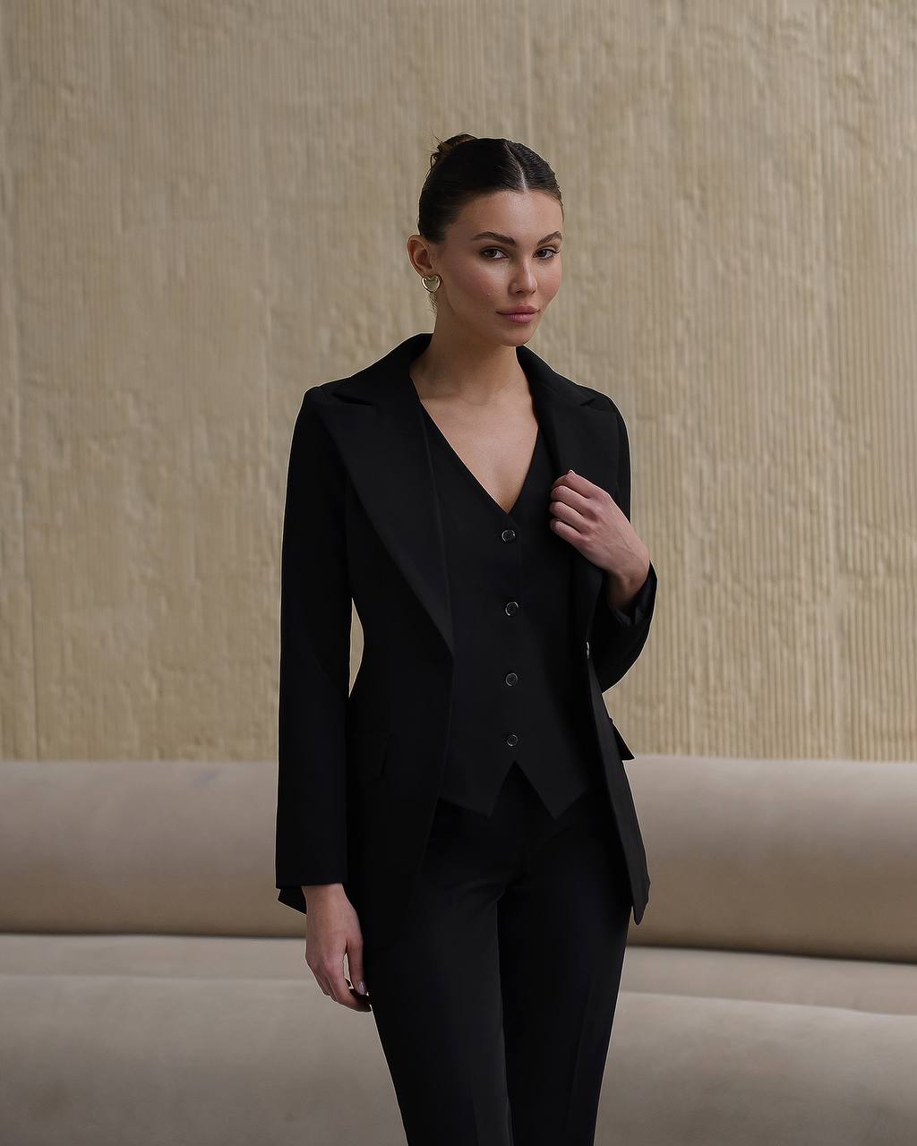 Woman wearing a black suit against a beige wall.