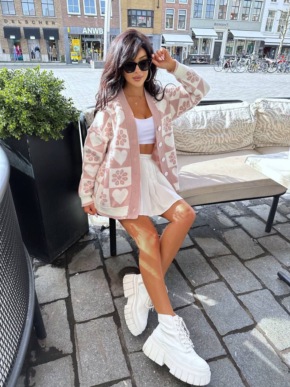 Woman in a floral cardigan, white skirt, and white sneakers standing on a city street.