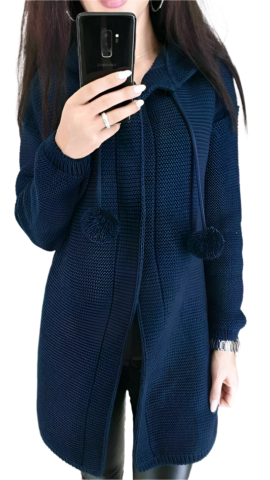Person wearing a blue knitted cardigan with pom-pom details, holding a phone.