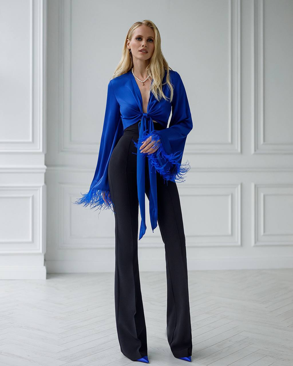 Woman wearing a blue top and black pants in a white room