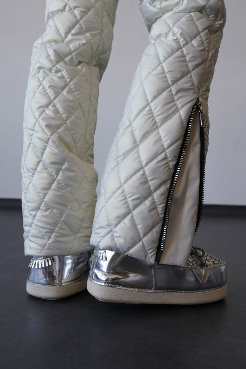 Quilted silver pants with zippers and metallic shoes on a dark floor.