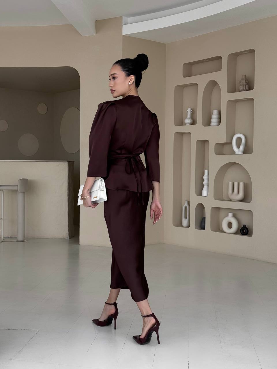 Woman in a brown outfit standing in a modern room with shelves.