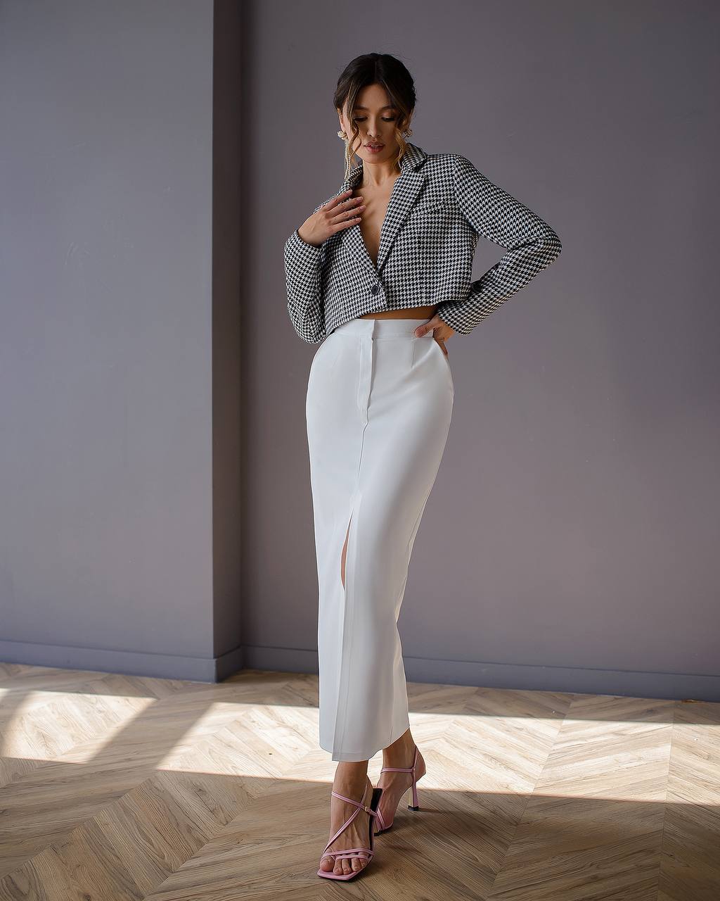 Woman wearing a checkered blazer and white pants in a room with wooden flooring.