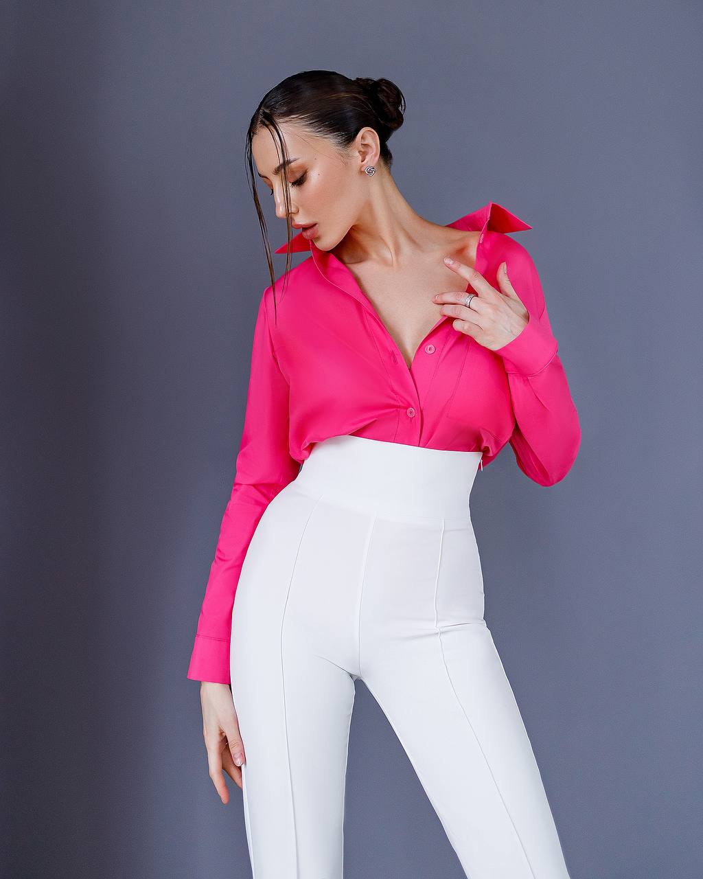 Woman wearing a bright pink blouse and white pants against a gray background
