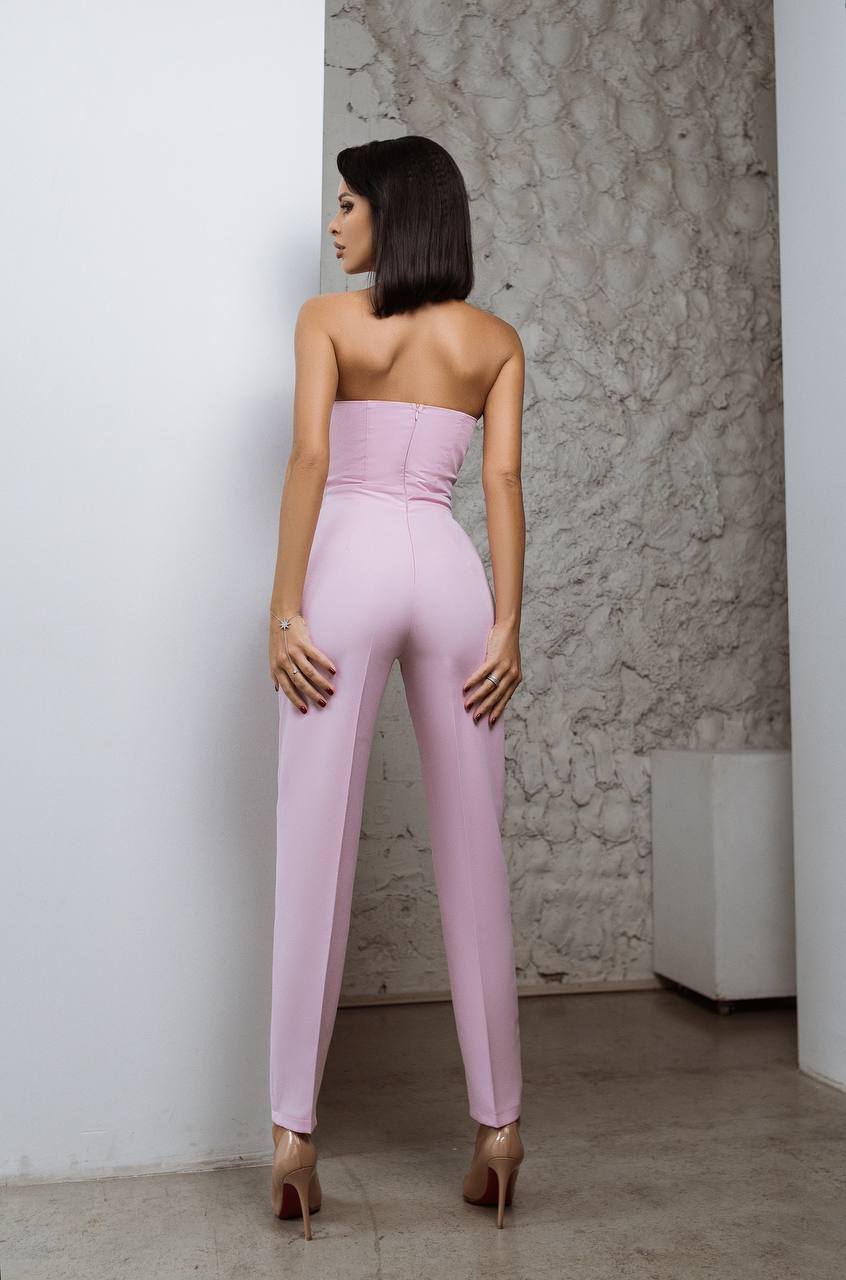 Woman wearing a pink strapless jumpsuit standing against a textured wall.