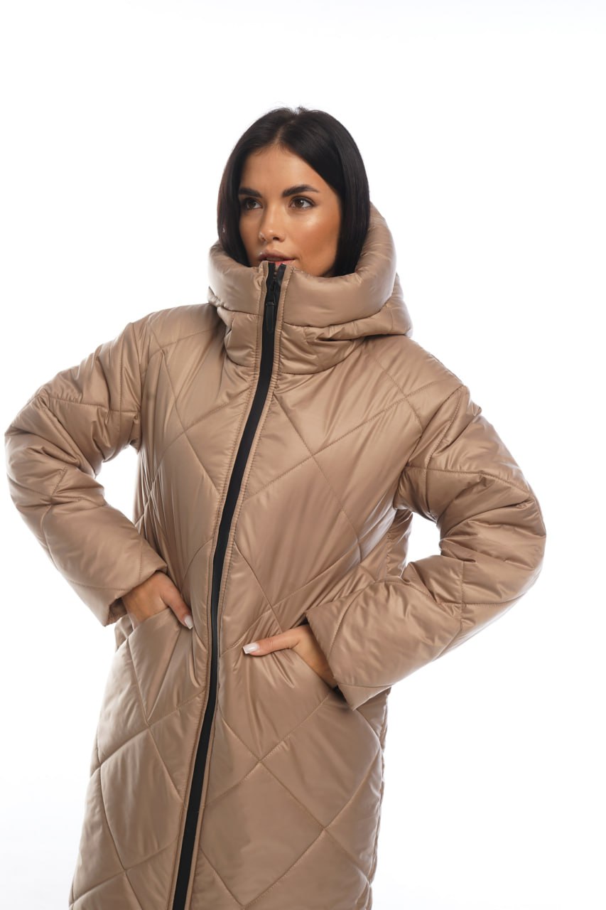 Woman wearing a beige quilted coat with a black zipper on a white background
