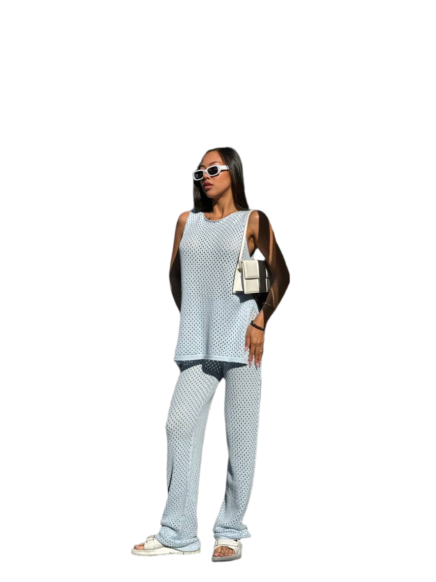 Woman wearing a light blue sleeveless top and pants with sunglasses and a handbag on a white background