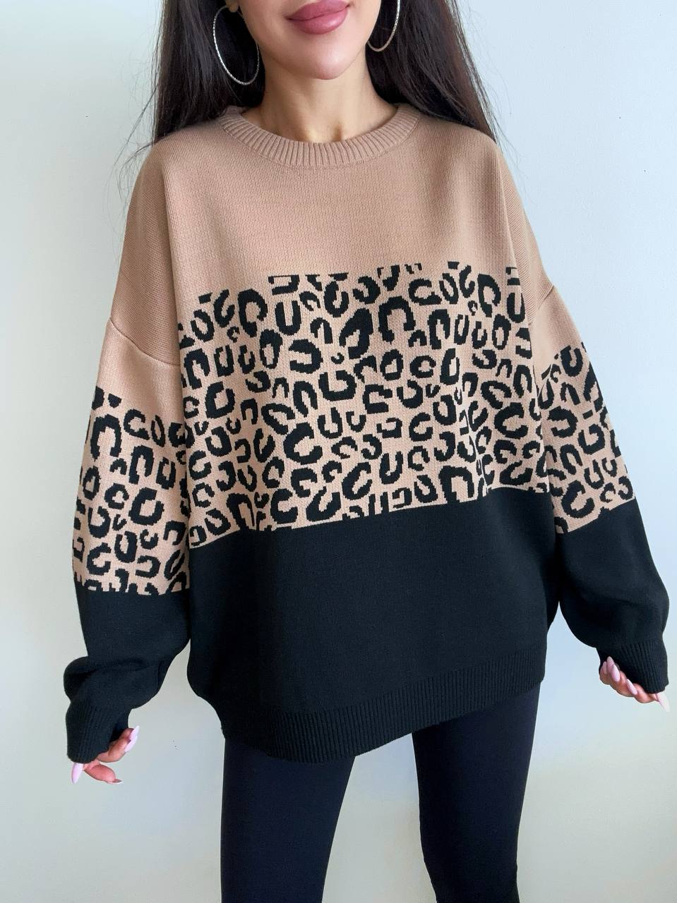 Person wearing a beige sweater with leopard print sleeves and black bottom half on a white background