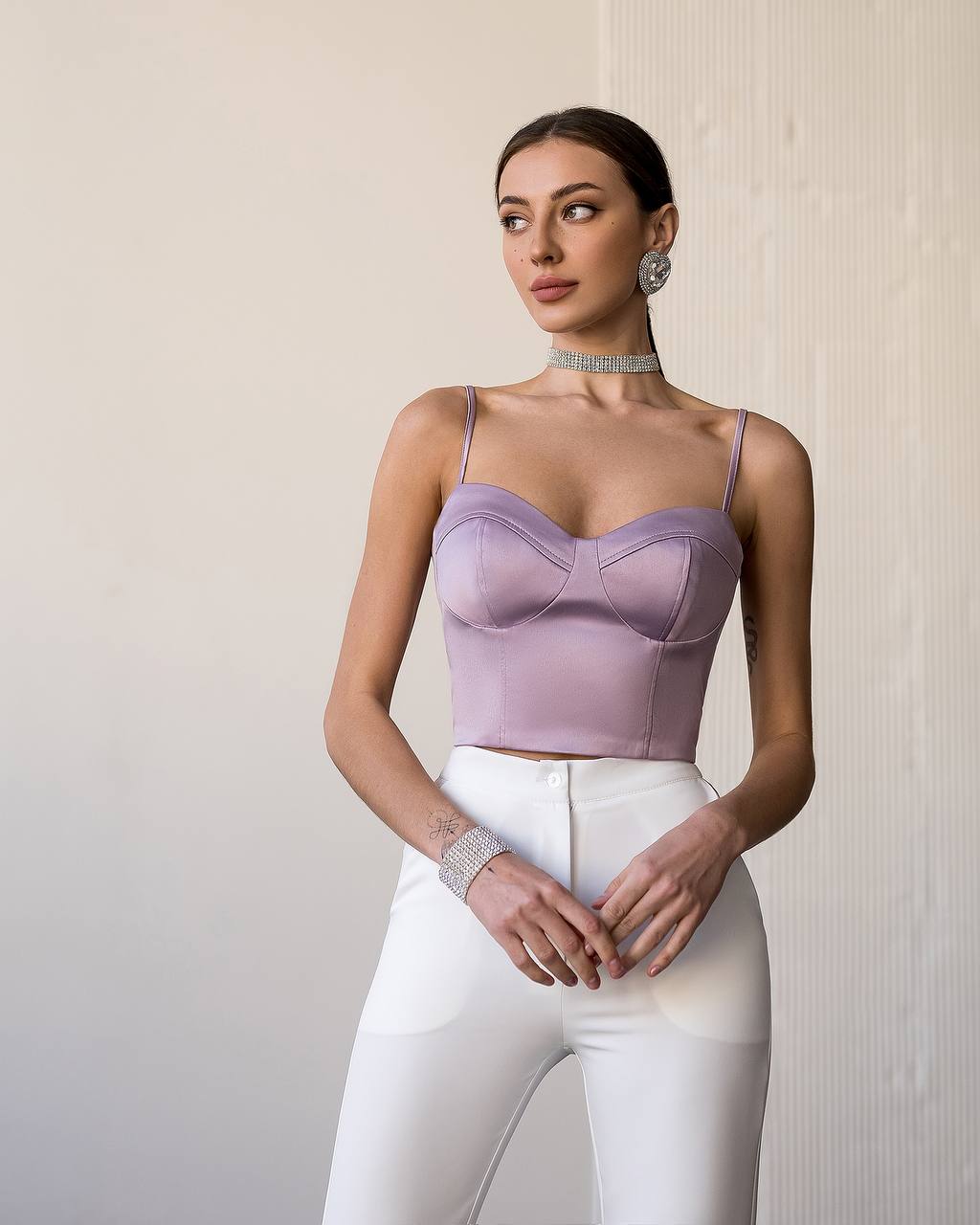 Woman wearing a lavender top and white pants against a neutral background