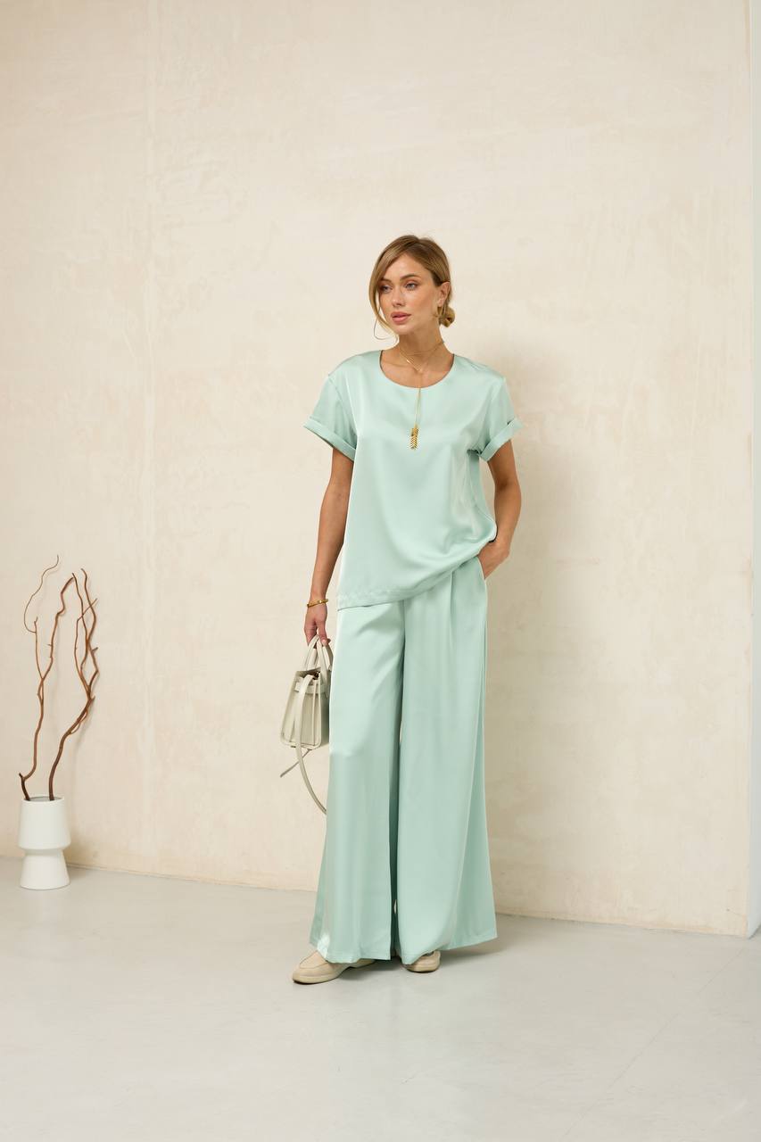 Woman wearing a light green outfit with wide-leg pants against a plain background