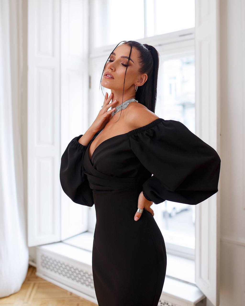 Woman wearing a black off-shoulder dress with puffed sleeves in a bright room.