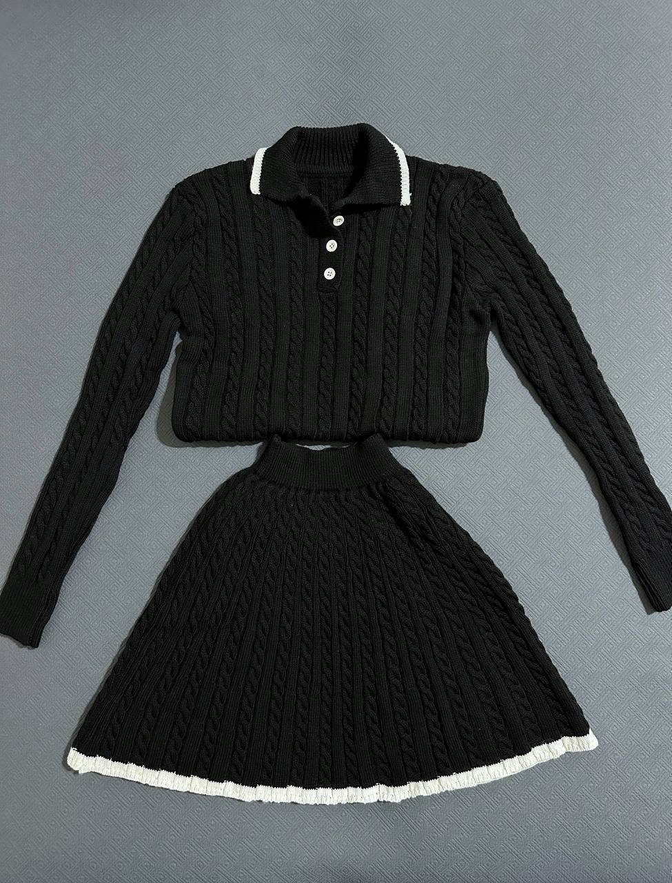 Black knitted sweater and skirt set on a gray background