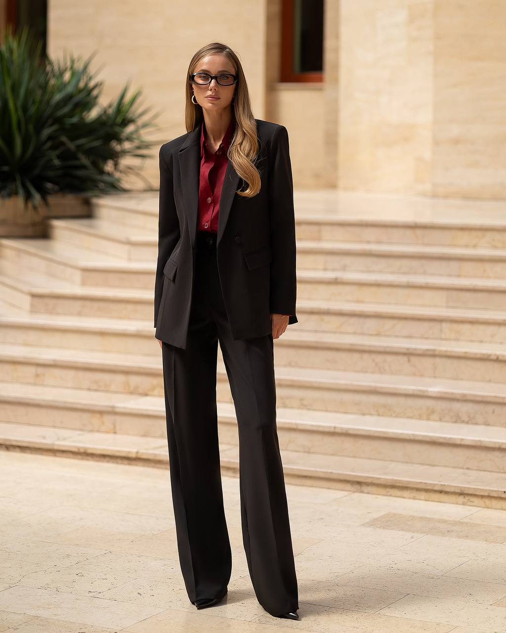 Woman in a black suit standing on stone steps with a building in the background
