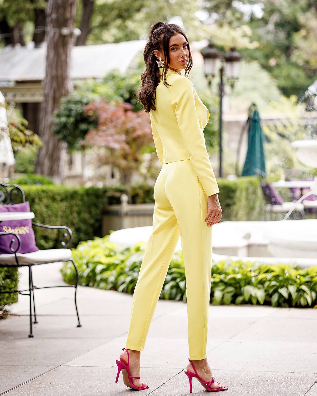 Woman in a yellow suit standing outdoors with greenery in the background