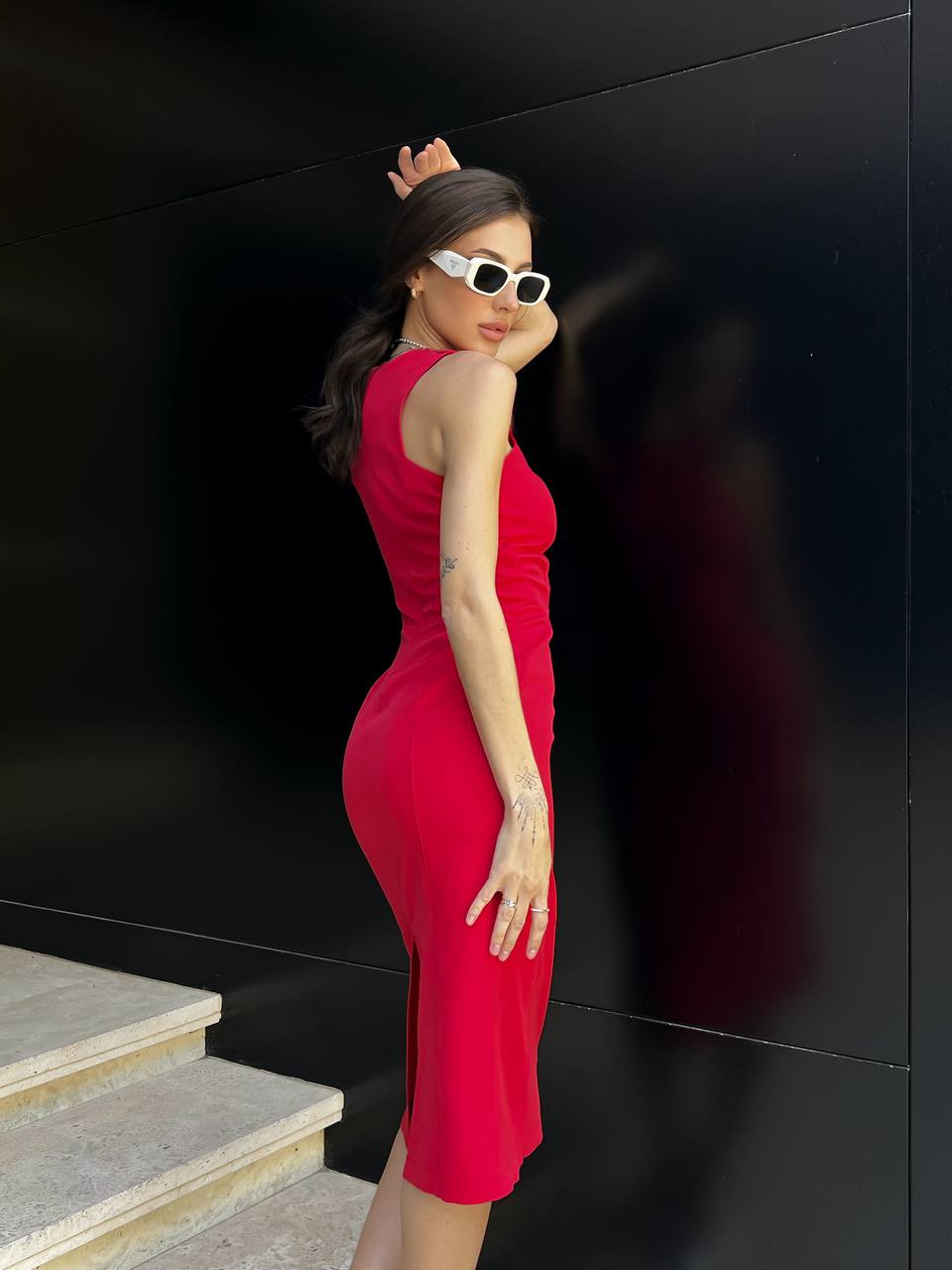 Woman in a red dress posing against a black wall.
