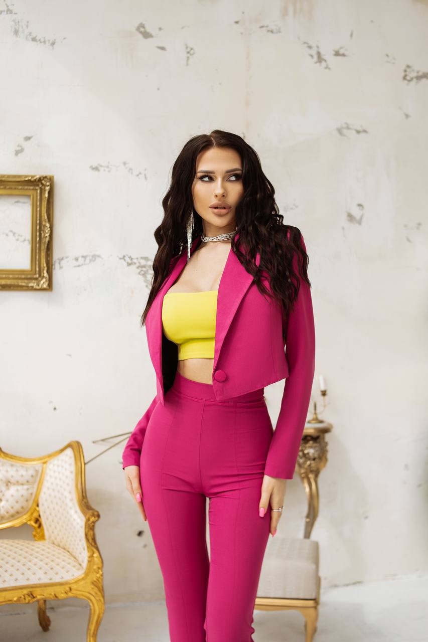 Woman in a pink outfit with a yellow top standing in an elegant room.