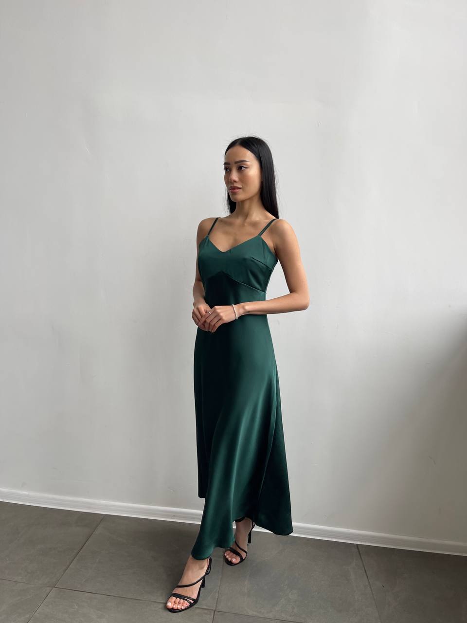 Woman wearing a green dress standing against a plain white wall.