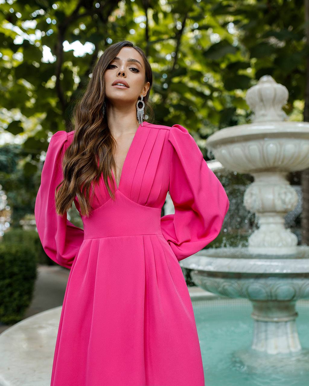 Woman in a pink dress standing in front of a fountain with greenery.